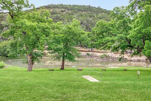Une zone herbeuse avec des arbres, une rivière et, au loin, une colline rocheuse.