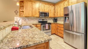 Eine Küche mit Holzschränken, einem Edelstahl-Kühlschrank, einer Mikrowelle, einem Backofen und Granit-Arbeitsplatten.