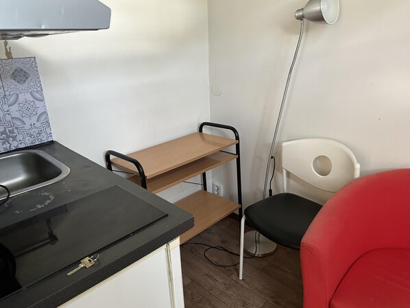 A kitchenette with a sink, a wooden shelf, a chair, and a red chair.