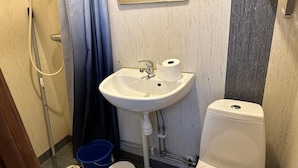 A bathroom with a white sink, two faucets, a toilet, a blue bucket, and a shower hose. - Apartment in Rosersberg Arlanda Airport (Rosersberg)