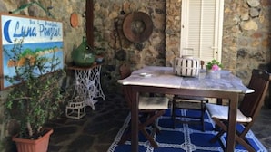 A stone-walled patio with a table and chairs, a potted plant, and a sign. - Sea Hedgehog Studio (Ponza)