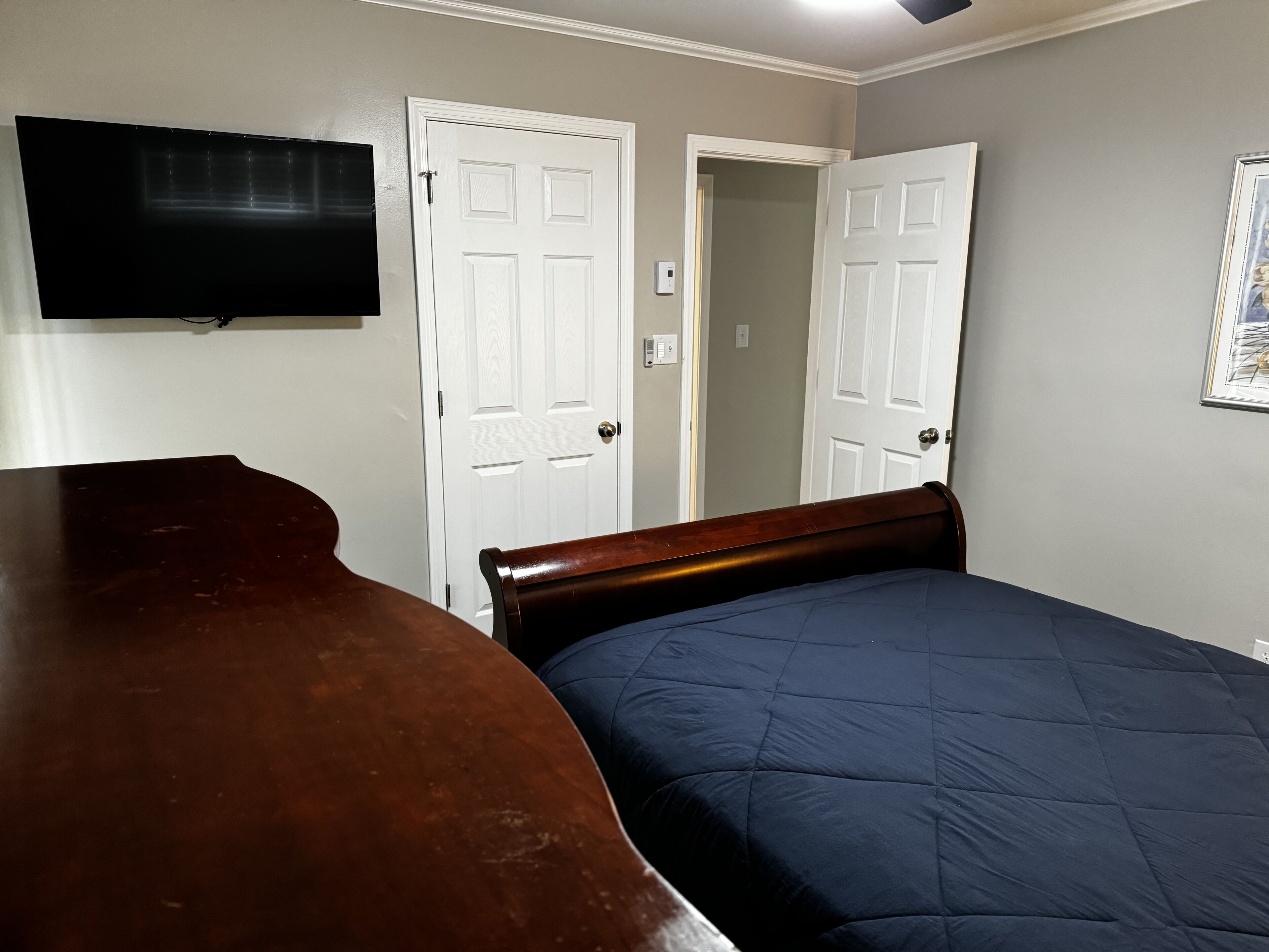 A bedroom with a bed, a dresser, a television mounted on the wall, and two doors.