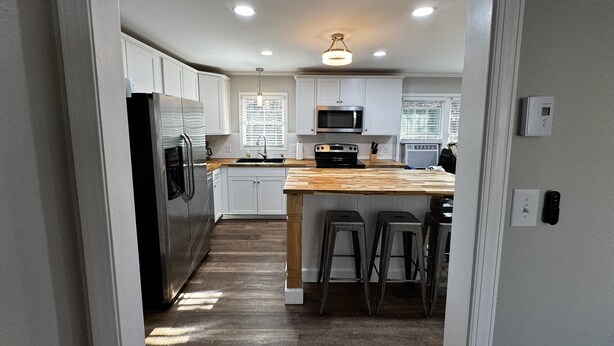 A modern kitchen with white cabinets, stainless steel appliances, and a wooden island with bar stools. - 3-bedroom vacation home near Cape Fear River (Lillington)