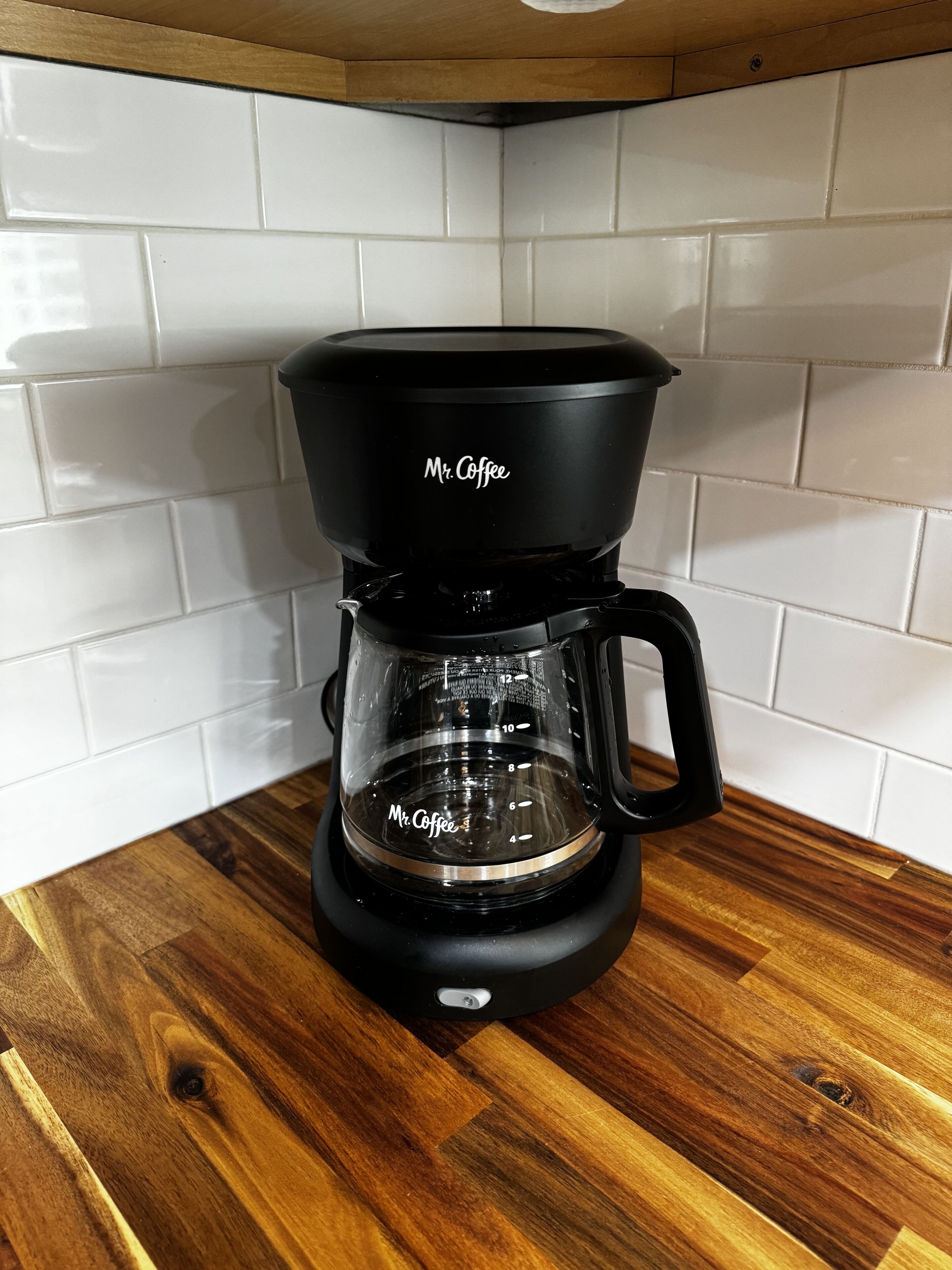A black Mr. Coffee coffee maker on a wooden countertop with white tiled backsplash.