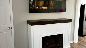 A living room with a fireplace, a mounted TV, and a door. - 3-bedroom vacation home near Cape Fear River (Lillington)
