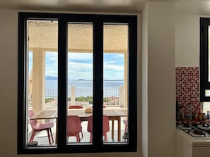 Uma cozinha com vista para uma varanda, área de refeições com cadeiras e painel de azulejos.