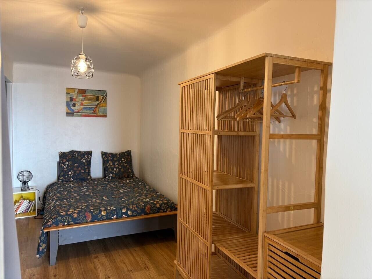 Ein Schlafzimmer mit einem Bett, einem Holzschrank, einer Hängeleuchte und einem Bücherregal.