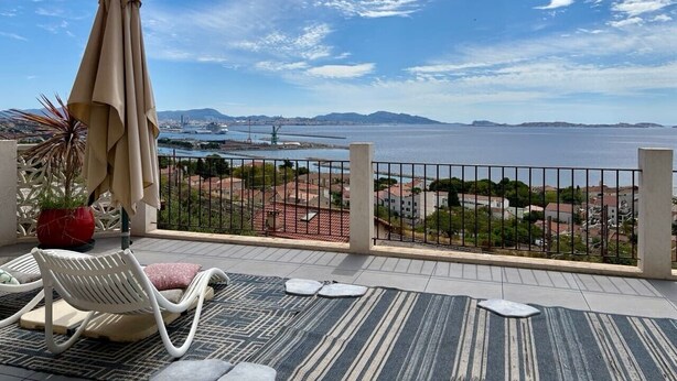 Un balcón con vista al mar, una silla, una mesa y una planta en maceta.