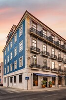 Un edificio de varios pisos con fachada azul, múltiples balcones y una entrada a nivel de calle con plantas en macetas.