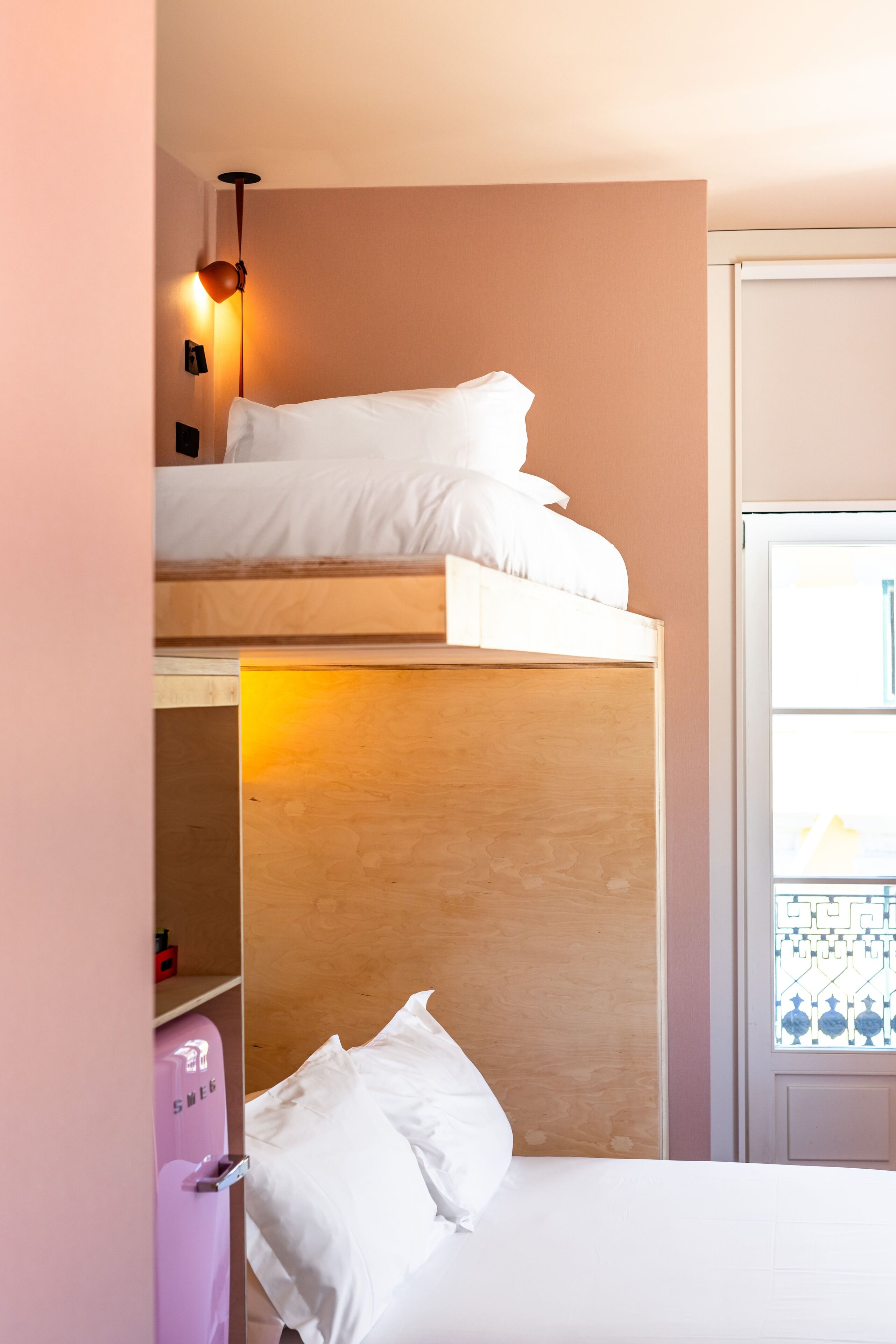 A bunk bed room with a wooden headboard, a pink suitcase, and a window with a view.