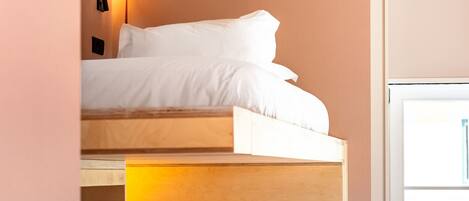 A bunk bed room with a wooden headboard, a pink suitcase, and a window with a view.