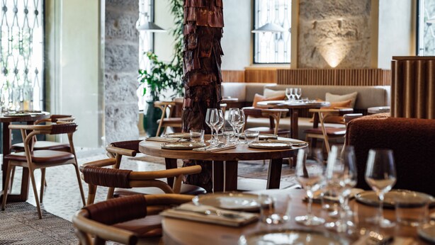 Un restaurante con mesas redondas dispuestas para comer, sillas de madera y un tocón de árbol como centro de mesa.