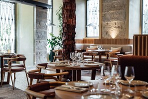 A restaurant with round tables set for dining, wooden chairs, and a large tree trunk centerpiece. - Independente Bica (Lisbon)