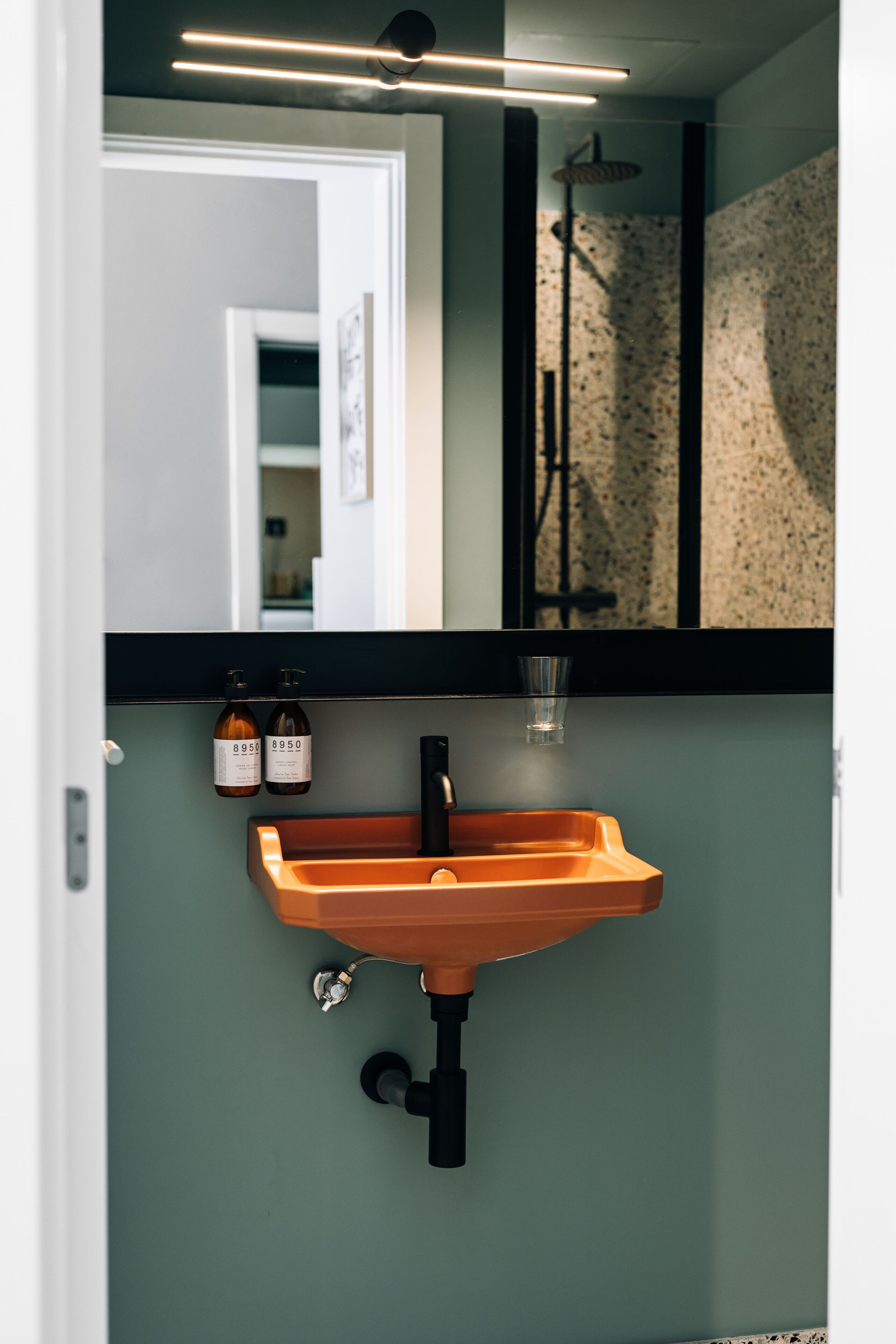 A bathroom with a modern sink, two bottles of hand soap, and a showerhead.