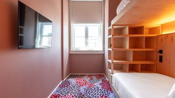 Ein kleines Hotelzimmer mit Bett, Wandfernseher und Fenster.