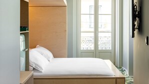 Habitación de hotel con cama, armario, espejo y ventana con vistas a edificios.