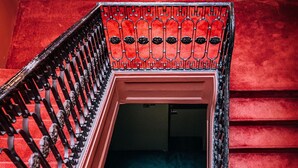 Una escalera con barandales de metal decorados y una pared roja.