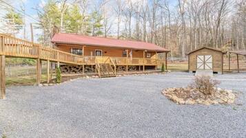 A rustic lodge with a gravel driveway, wooden deck, and a small shed.