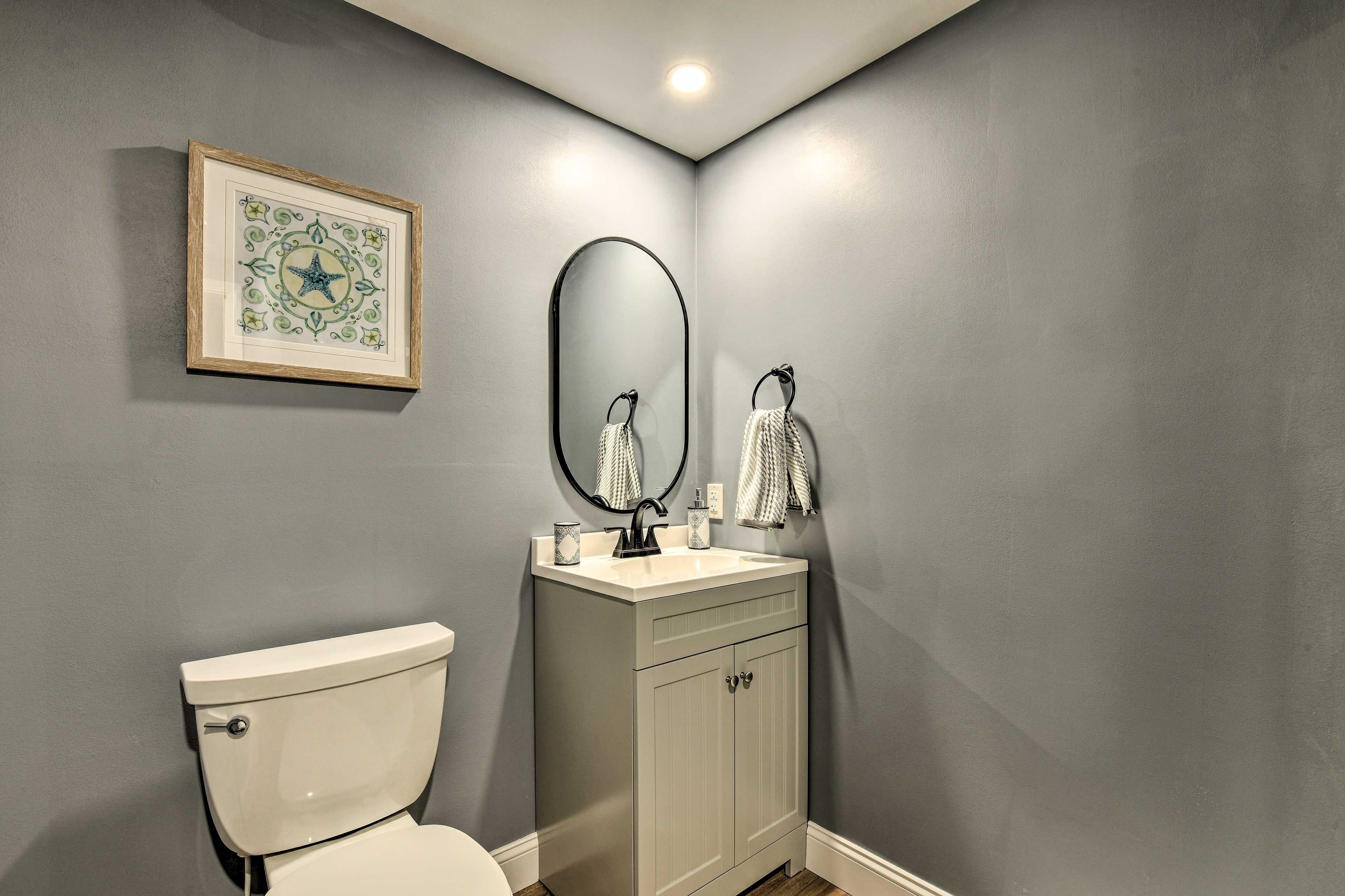 A bathroom with a toilet, a sink with a mirror, and a framed artwork on the wall.