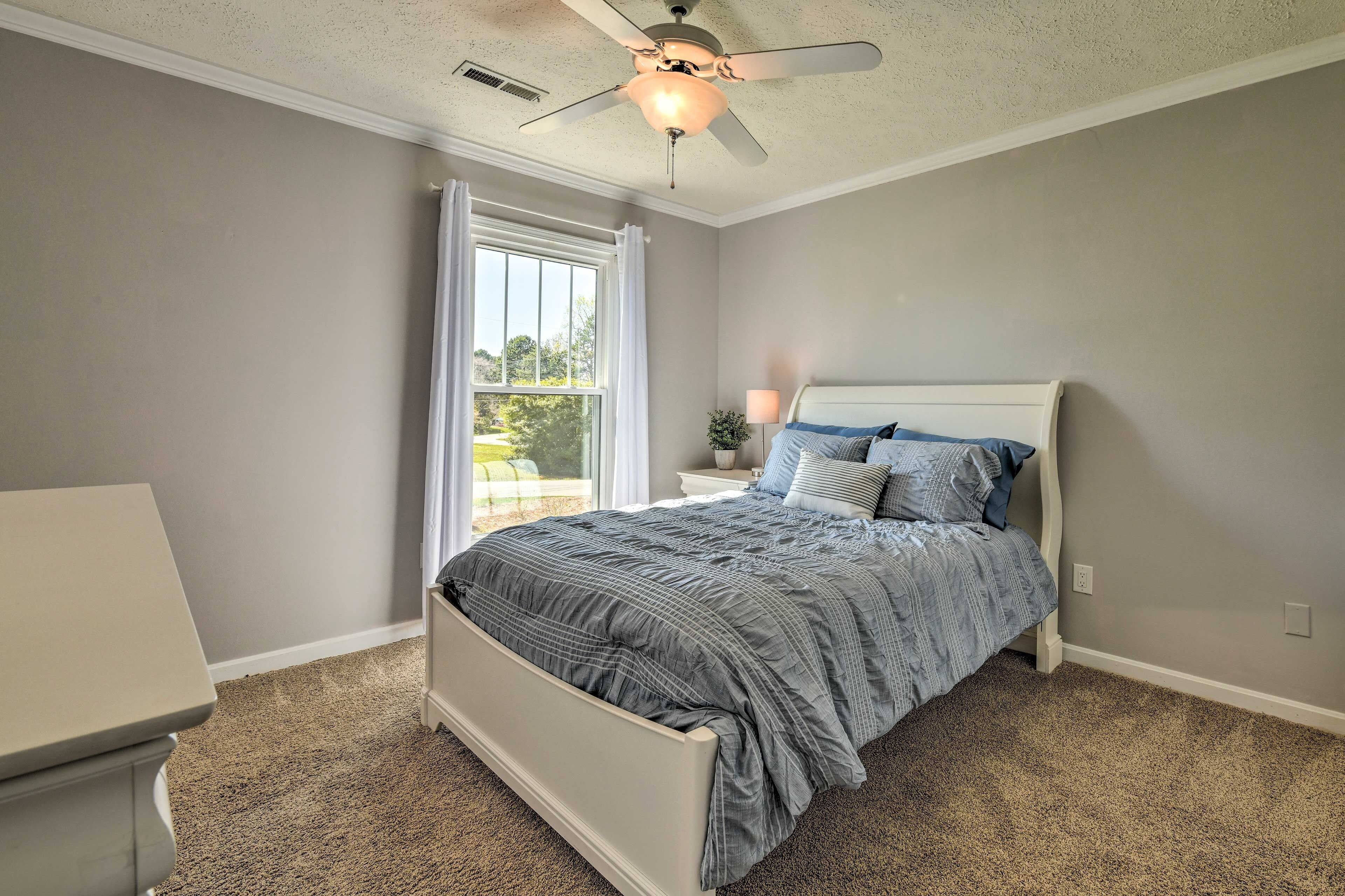 Une chambre à coucher avec un lit, un ventilateur de plafond, une fenêtre et une table de chevet.