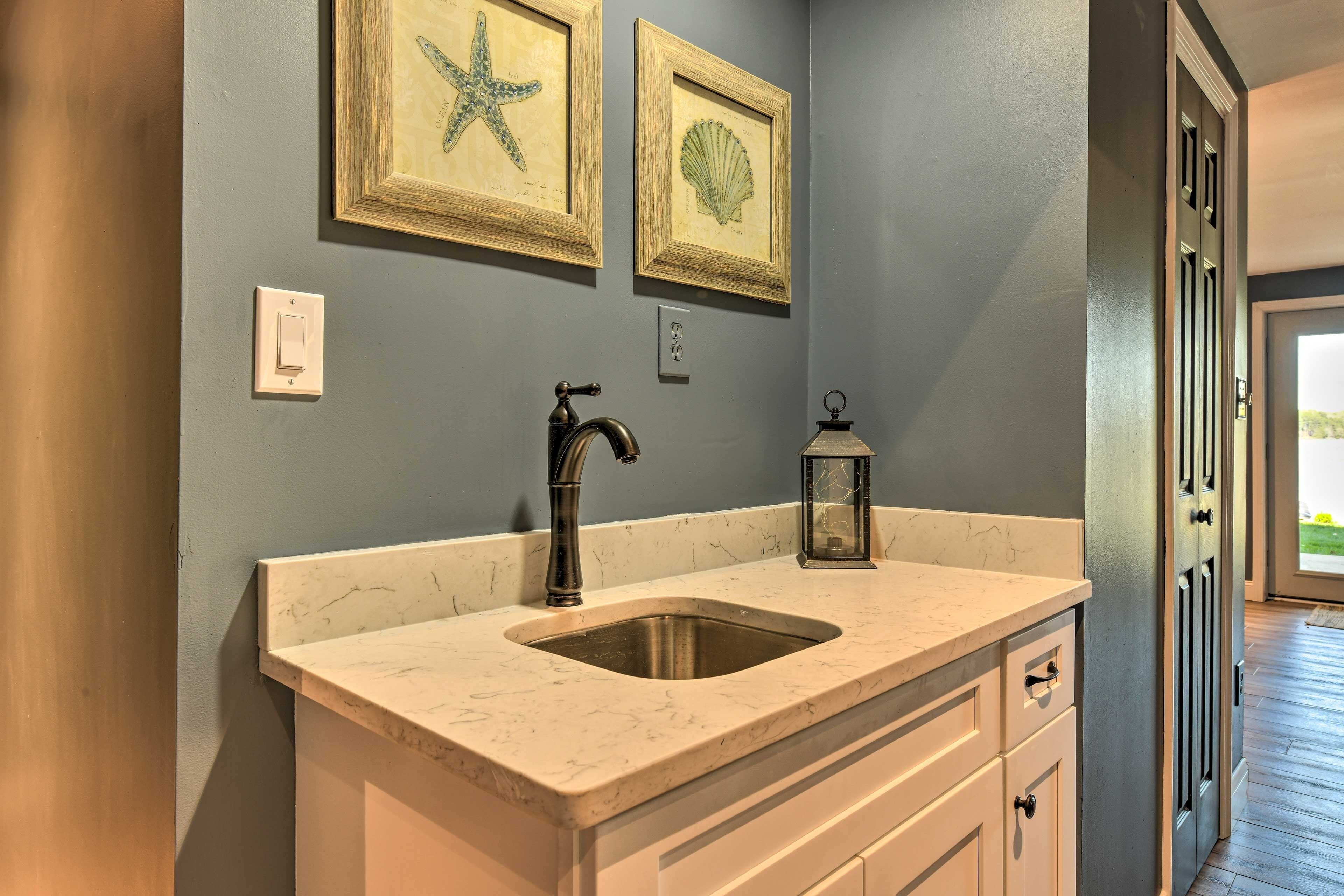 A kitchen with a marble countertop, a sink, a faucet, and a lantern. There are framed pictures on the wall and a door to the right.