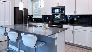 A modern kitchen with white cabinets, a central island with bar stools, stainless steel appliances, and pendant lighting. - 5 Bed 5 Bath South Facing Pool Home Storey Lake 5 Bedroom Home by RedAwning (Kissimmee)