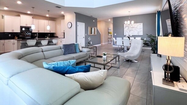 A spacious living area with a curved sofa, a coffee table, and a dining area with white chairs. - 5 Bed 5 Bath South Facing Pool Home Storey Lake 5 Bedroom Home by RedAwning (Kissimmee)