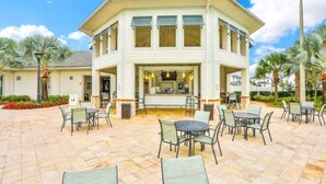 A two-story building with a patio area featuring outdoor seating and a central bar. - 5 Bed 5 Bath South Facing Pool Home Storey Lake 5 Bedroom Home by RedAwning (Kissimmee)