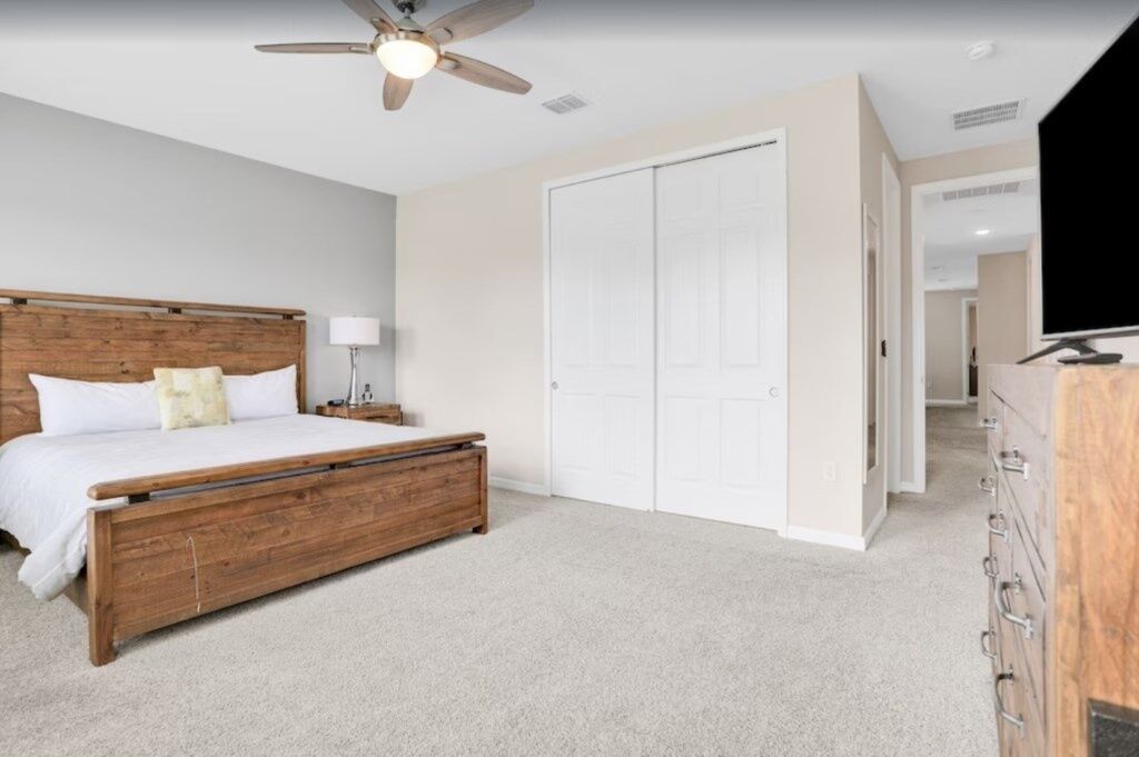 A bedroom with a wooden bed, a ceiling fan, a white wardrobe, and a television.