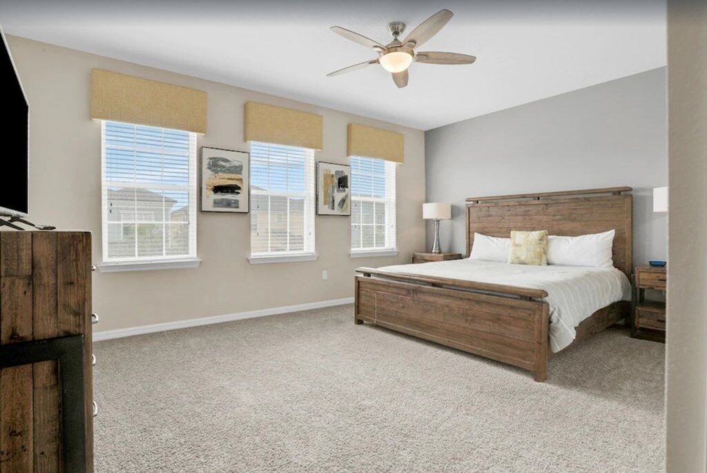 A bedroom with a wooden bed, a ceiling fan, and three windows with blinds.