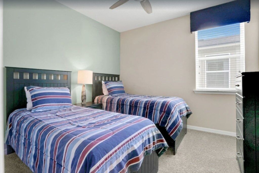 A bedroom with two beds, a nightstand with a lamp, a dresser, and a window with blinds.