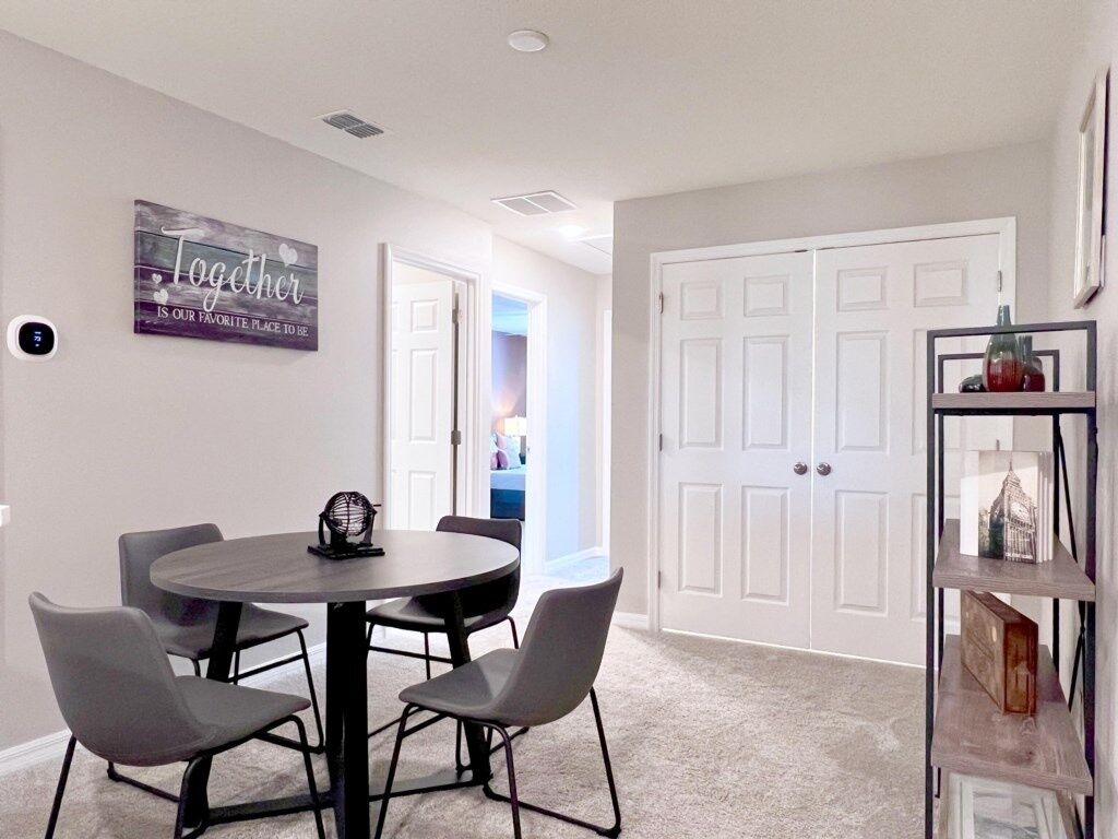 A dining area with a round table and four chairs, a white door, and a shelf with decorative items.