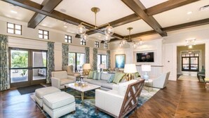 A spacious living room with a high ceiling, large windows, and a modern chandelier.