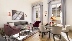 Una sala de estar moderna con un sofá gris, un sillón rojo, una mesa de comedor con sillas y un ventanal con cortinas.