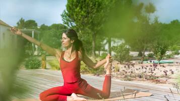 Una persona vestida de rojo realizando una postura de yoga sobre una cubierta de madera, con un jardín al fondo.