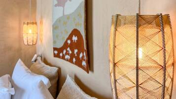 Un dormitorio con cama, almohadas, una obra de arte colgada en la pared y una lámpara de fibra.