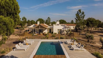 A pool area with lounge chairs and a house in the background.