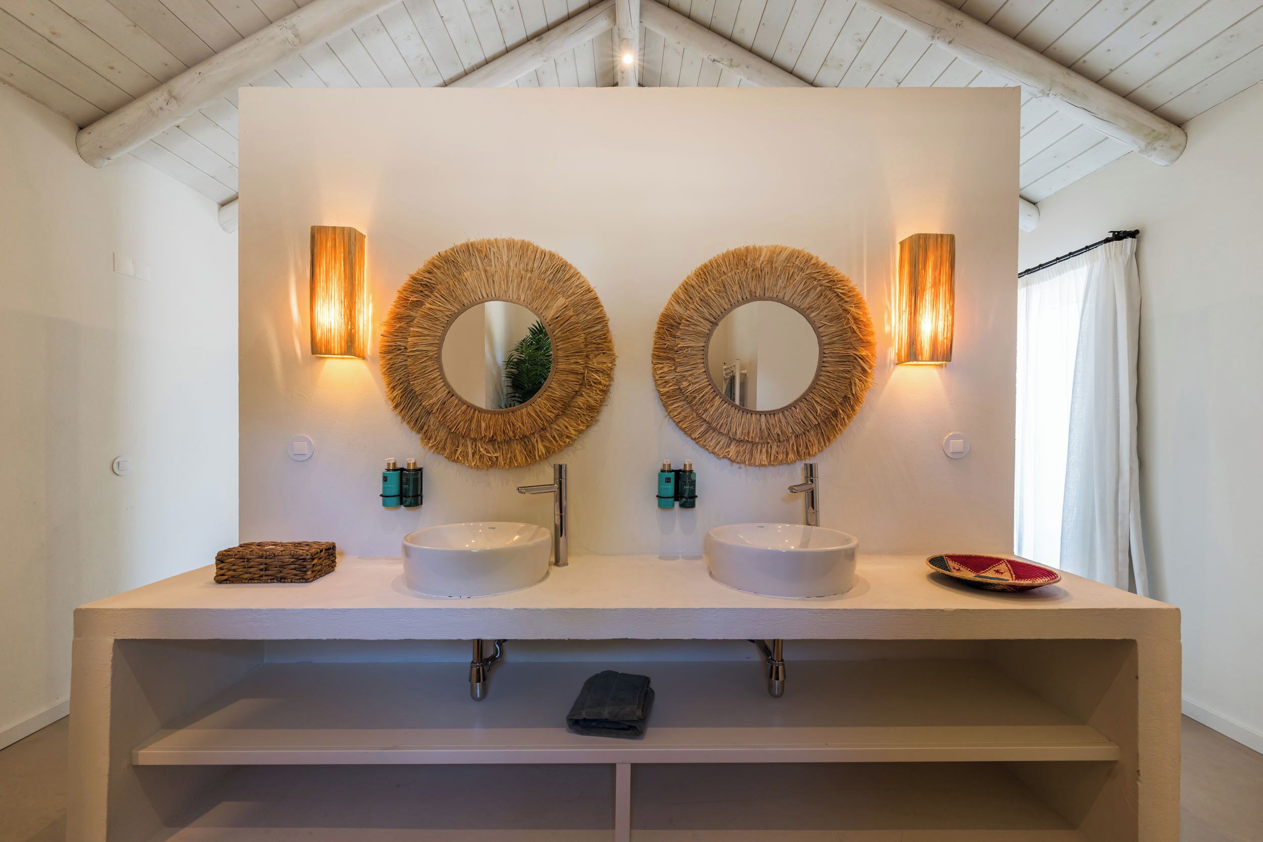 A bathroom with two round mirrors, a white sink, and a shelf below.