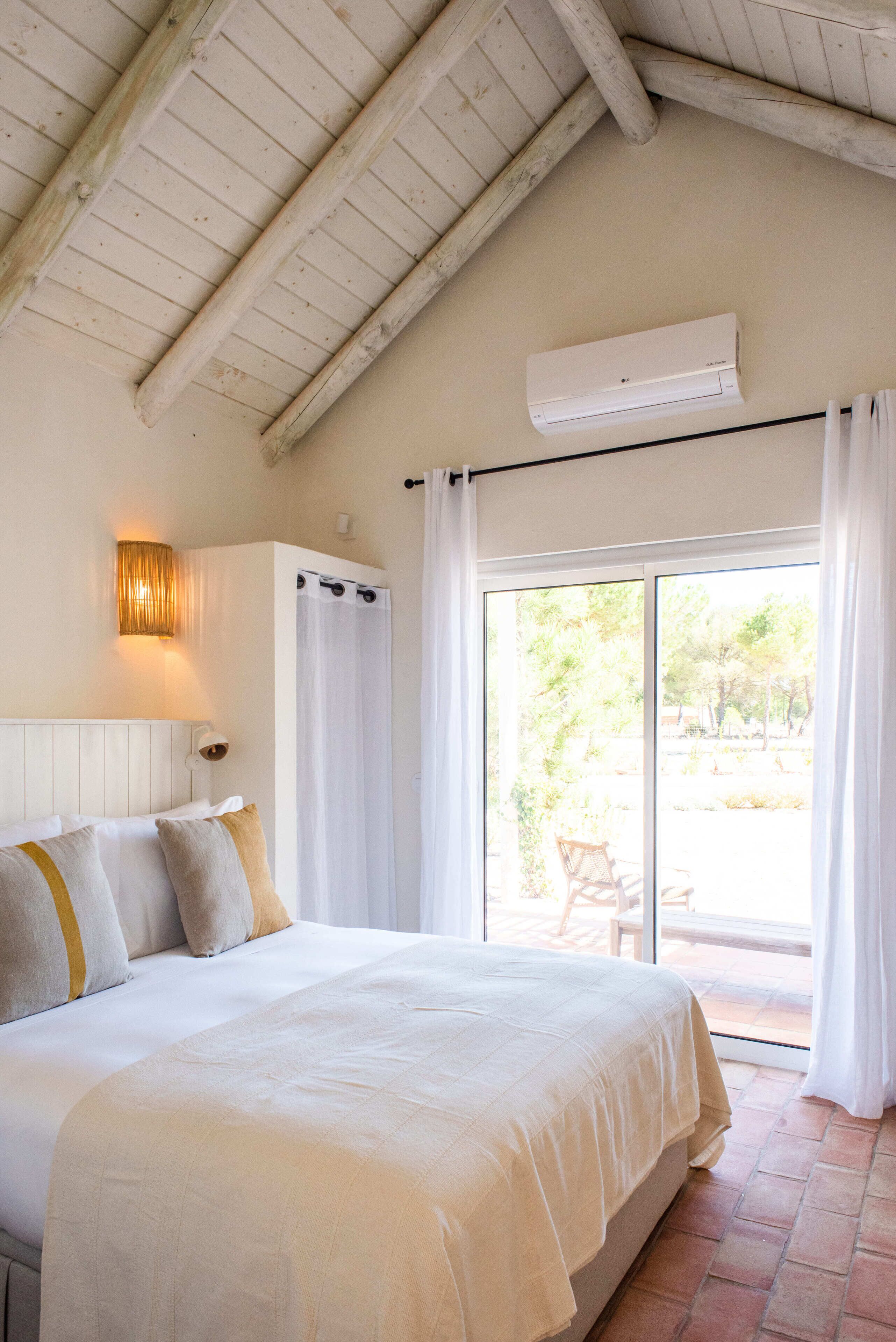 A bedroom with a large bed, a ceiling fan, an air conditioning unit, and a sliding glass door leading to an outdoor area.