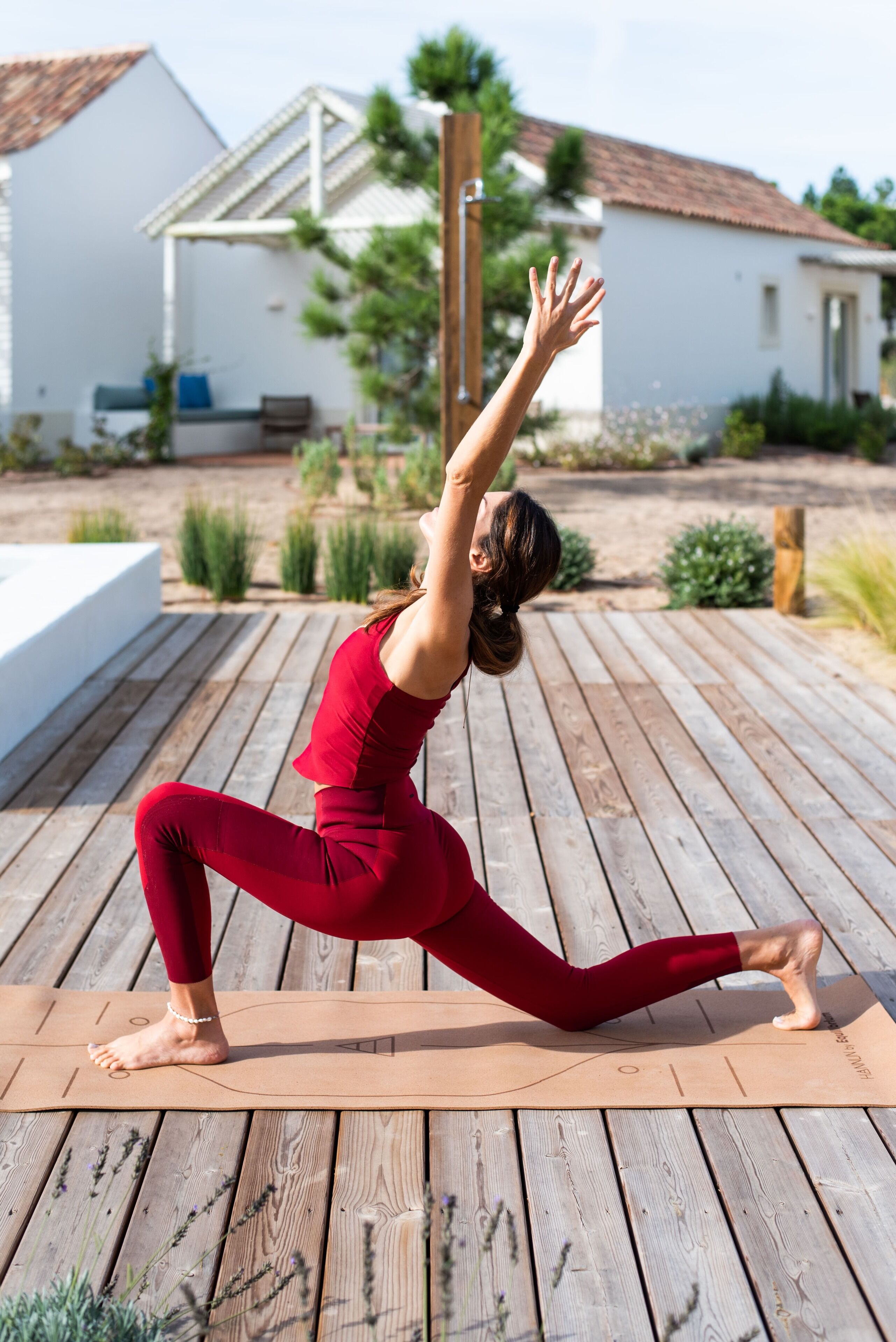 Una persona realizando una postura de yoga sobre una terraza de madera, con una casa al fondo.