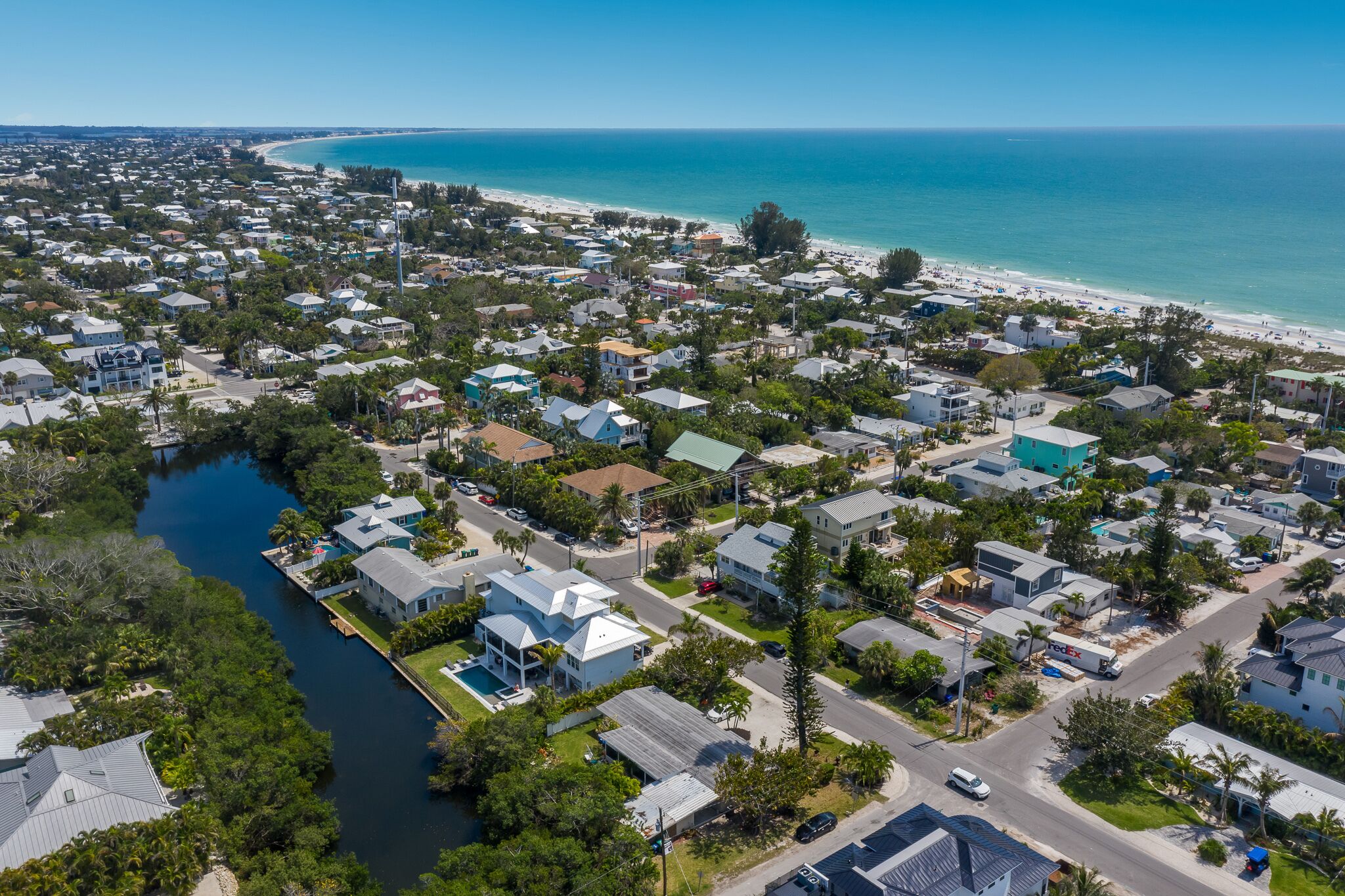 An aerial view of a coastal residential area with houses, a river, and a beach.