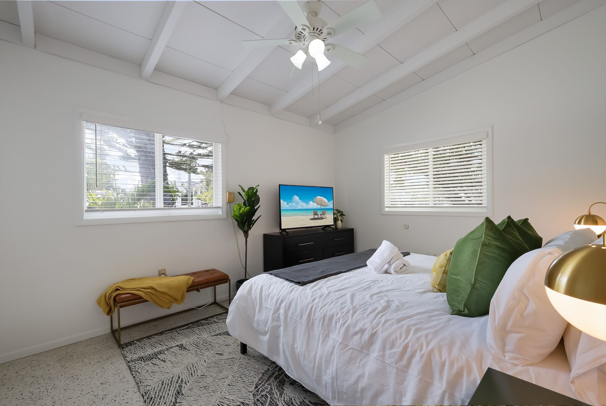 A bedroom with a bed, a bench, a TV, and a ceiling fan.