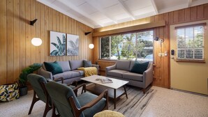 A cozy living room with wooden walls, two sofas, a coffee table, and a door with blinds.