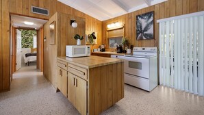 A kitchen with wooden cabinets, a microwave, a stove, and a sink. There is a window with blinds and a plant on the counter.