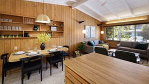 A modern living room with a wooden dining area, a ceiling fan, and large windows.