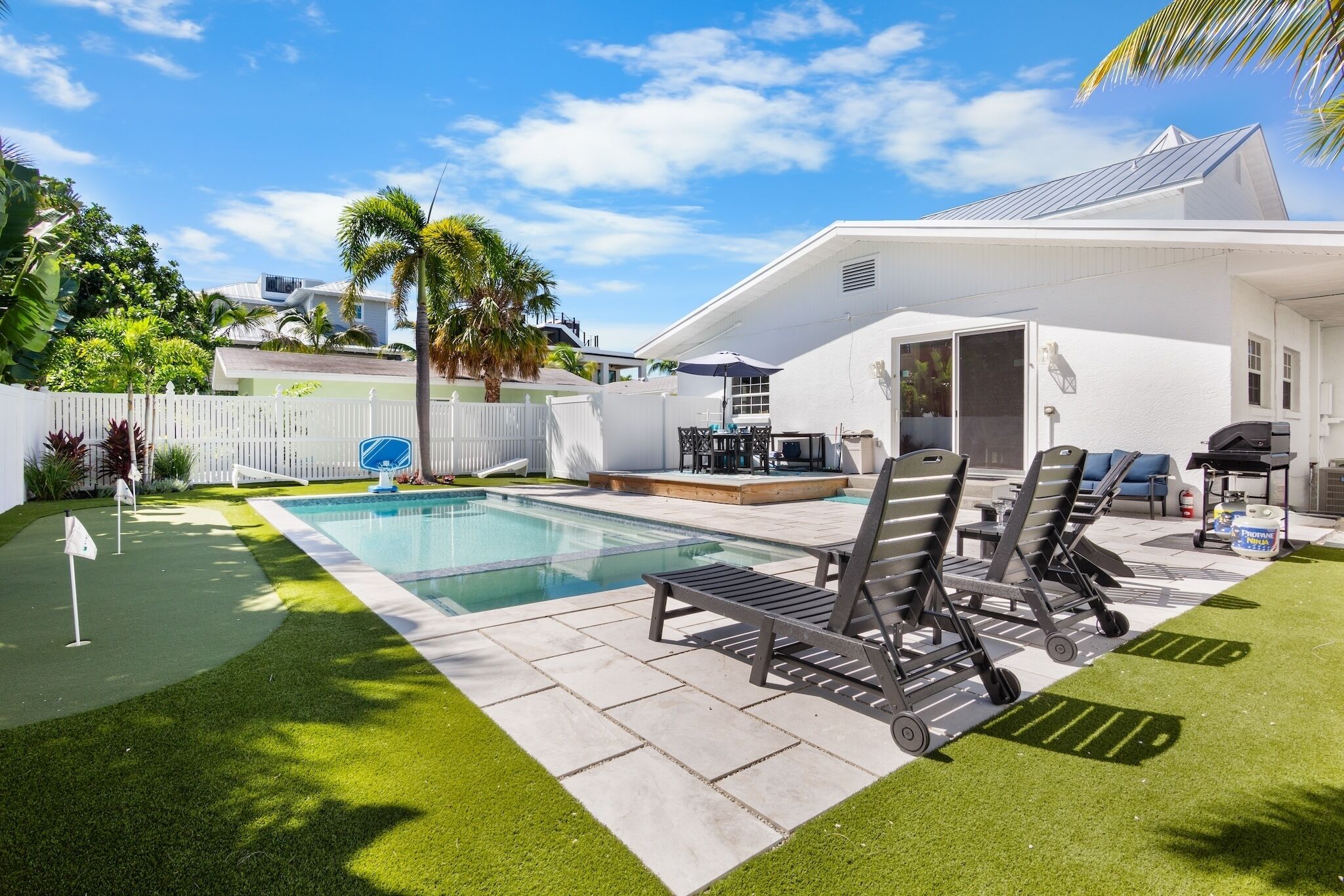 Ein Garten mit Swimmingpool, Liegestühlen und Grillplatz.