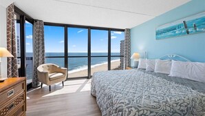 A bedroom with a large bed, a chair, a dresser, and a view of the ocean. - Golden Sands 1517 by Seaside Vacations & Sales (Ocean City)