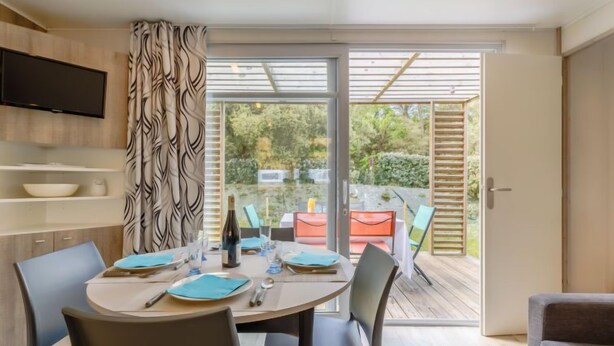 Un comedor con una mesa lista para cuatro, un televisor montado en la pared y vistas del jardín a través de puertas de vidrio.