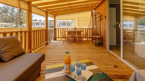 Una terraza de madera con un sofá, una mesa con bebidas y un área de comedor con sillas.