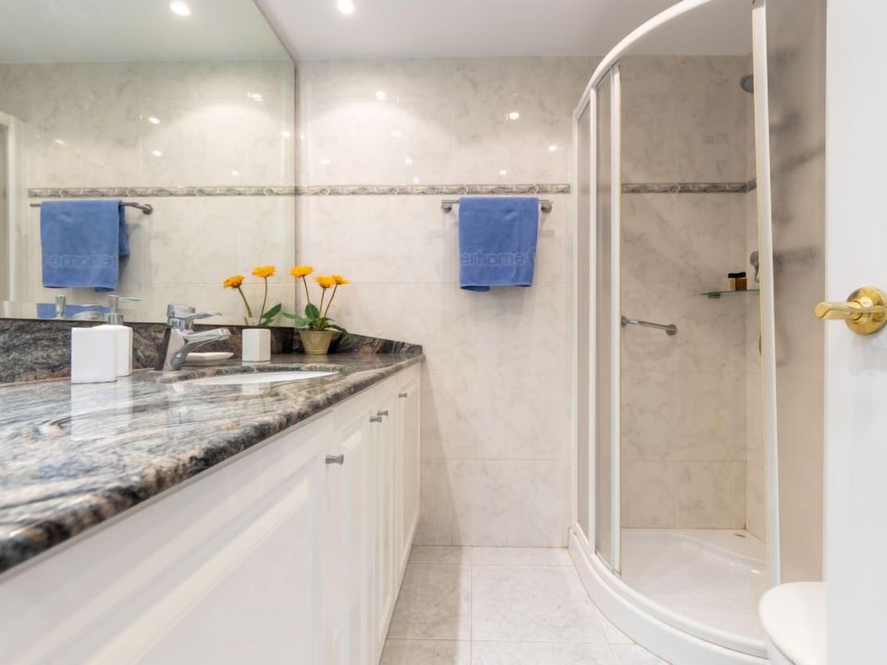 Ein modernes Badezimmer mit Dusche in Bogenform, Marmorplatten und zwei blauen Handtüchern, die an der Wand hängen.